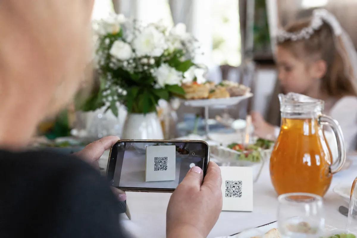 Gość skanuje telefonem kod QR z kartonika na stole, komunia