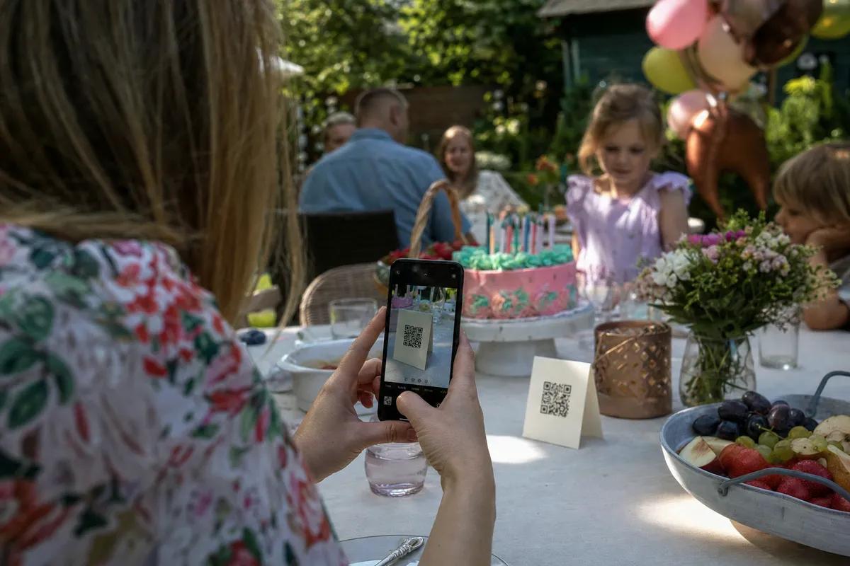 Gość skanuje telefonem kod QR z kartonika na stole, urodziny