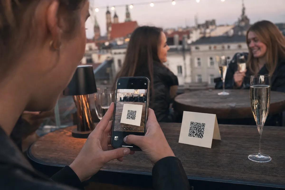 Gość skanuje telefonem kod QR z kartonika na stole, wieczór panieński